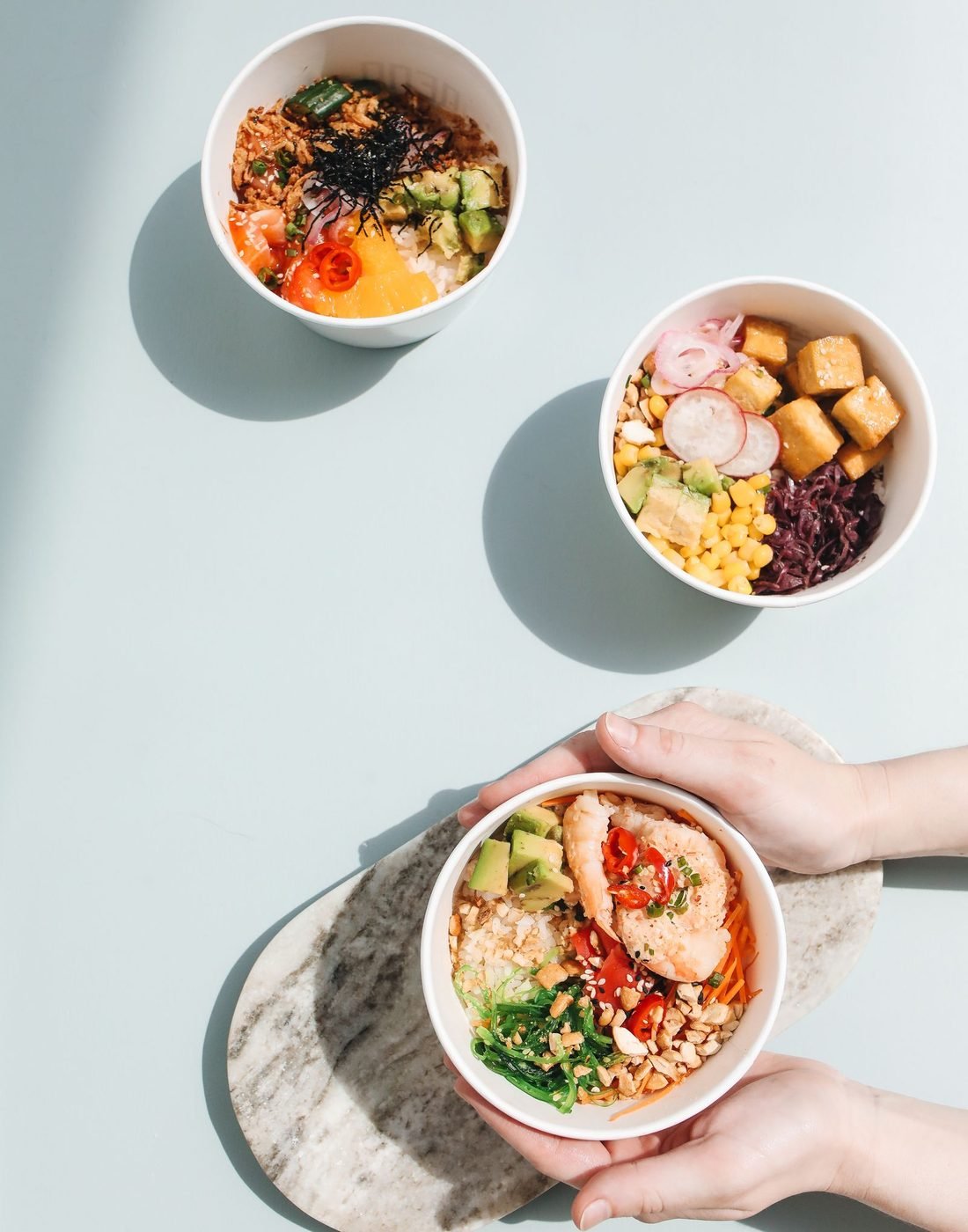Tres bowls de poke vistos desde arriba, uno sostenido con las manos